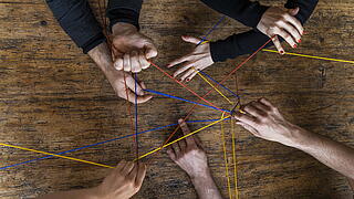 mehrere Hände die mit Fäden verwickelt sind