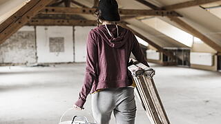 Person mit Leiter und Farbeimer auf einem Dachboden